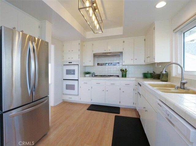 kitchen featuring decorative backsplash, stainless steel appliances, a sink, light wood-type flooring, and a raised ceiling