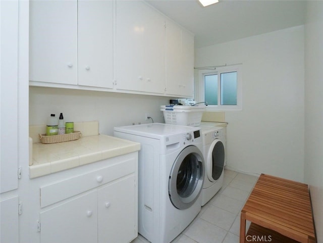 clothes washing area featuring light tile patterned floors, cabinet space, and washer and clothes dryer
