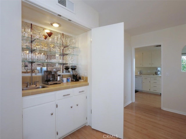 bar with a sink, white dishwasher, wet bar, and light wood-type flooring
