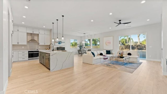 kitchen with white cabinets, appliances with stainless steel finishes, open floor plan, decorative light fixtures, and wall chimney range hood