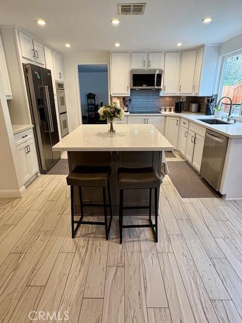 8373 Denise Ln, West Hills, CA 91304 - kitchen featuring appliances with stainless steel finishes, light wood-style flooring, light countertops, a kitchen breakfast bar, and white cabinetry