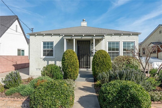 view of front facade with a chimney, stucco siding, a shingled roof, crawl space, and fence