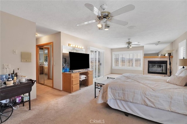 bedroom with multiple windows, light carpet, a tiled fireplace, and a textured ceiling