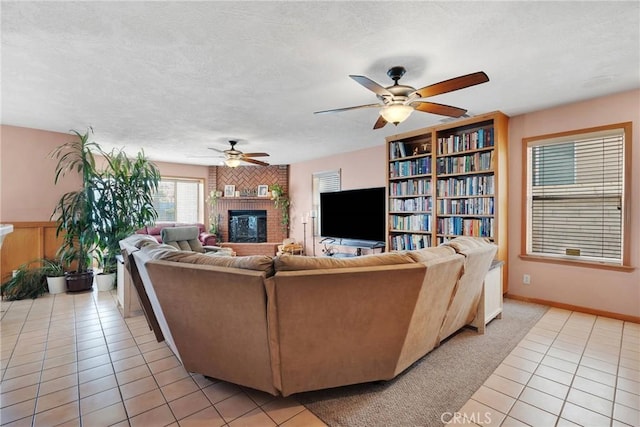 living room with a ceiling fan, a fireplace, a textured ceiling, and light tile patterned floors