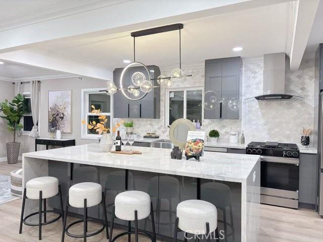 kitchen featuring light stone countertops, gray cabinetry, wall chimney range hood, pendant lighting, and gas stove