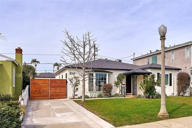 view of front of home with a front lawn, roof with shingles, fence, and stucco siding