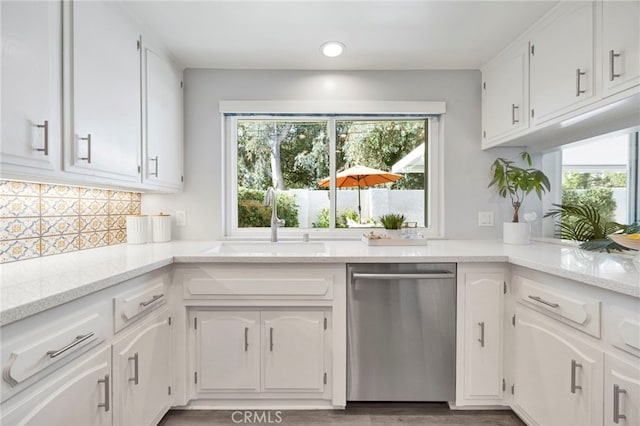 kitchen featuring white cabinets, backsplash, light stone countertops, stainless steel dishwasher, and a sink