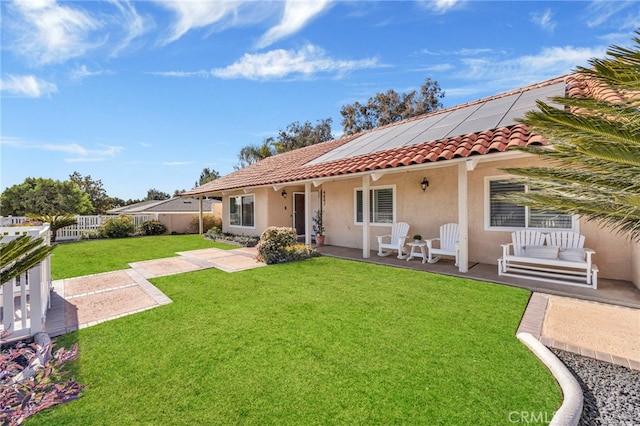 back of property with a tile roof, stucco siding, solar panels, a lawn, and fence