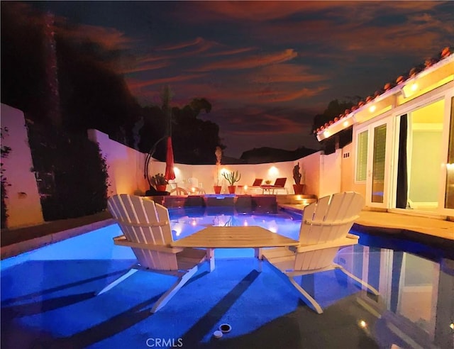 pool at night featuring a patio, an infinity pool, and a fenced backyard