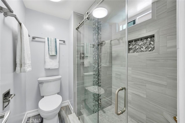 bathroom with toilet, a shower stall, and baseboards