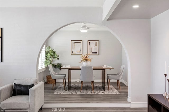 dining area with arched walkways, ceiling fan, baseboards, and wood finished floors