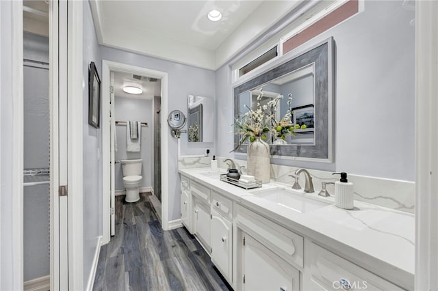 full bathroom with double vanity, visible vents, toilet, a sink, and wood finished floors