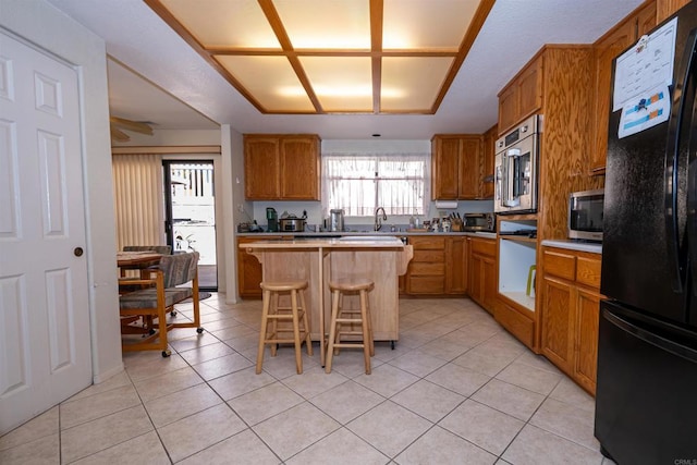 kitchen with freestanding refrigerator, a kitchen breakfast bar, a kitchen island, stainless steel microwave, and light countertops