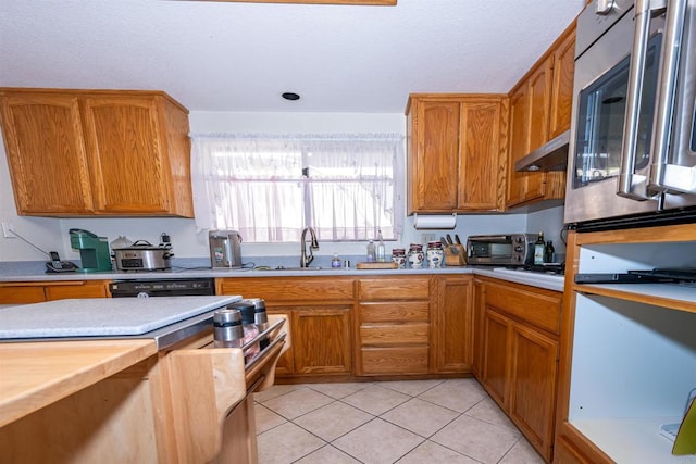 kitchen featuring stainless steel microwave, light tile patterned floors, light countertops, under cabinet range hood, and a sink