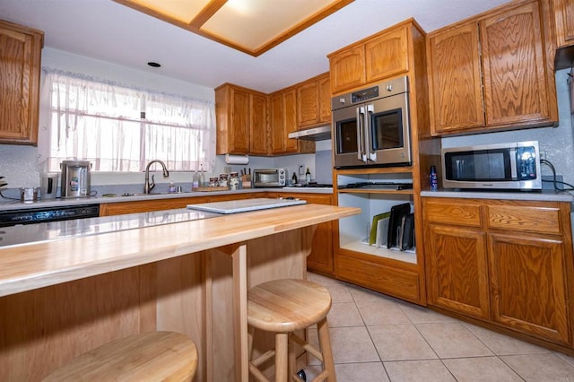 kitchen featuring a breakfast bar, butcher block counters, brown cabinetry, stainless steel appliances, and a sink