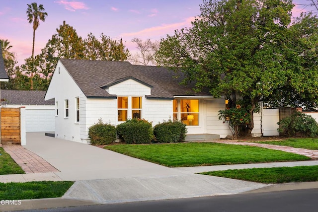 view of front of property with a shingled roof and a lawn