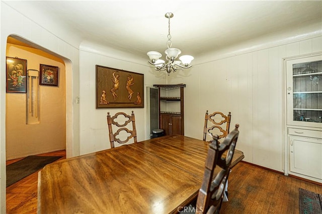 dining room with an inviting chandelier, arched walkways, and dark wood finished floors