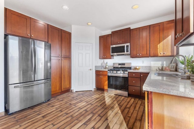 kitchen with light stone counters, recessed lighting, appliances with stainless steel finishes, dark wood-type flooring, and a sink