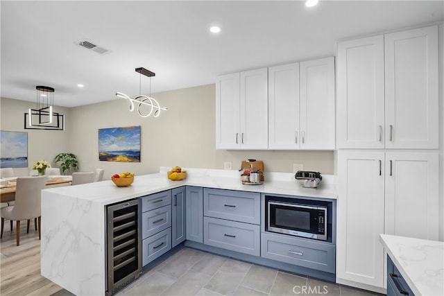 kitchen featuring beverage cooler, stainless steel microwave, white cabinetry, and pendant lighting