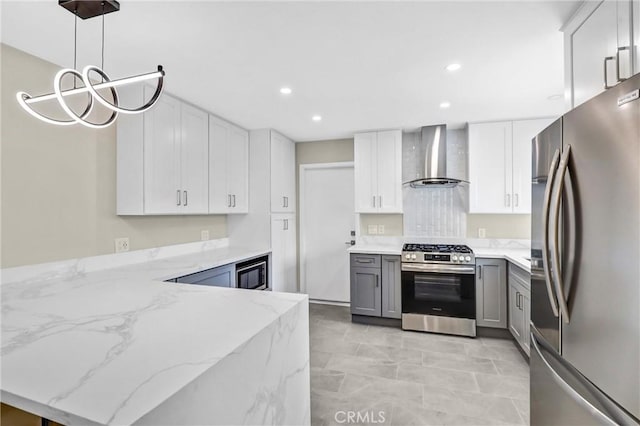 kitchen with appliances with stainless steel finishes, hanging light fixtures, light stone countertops, gray cabinetry, and wall chimney range hood