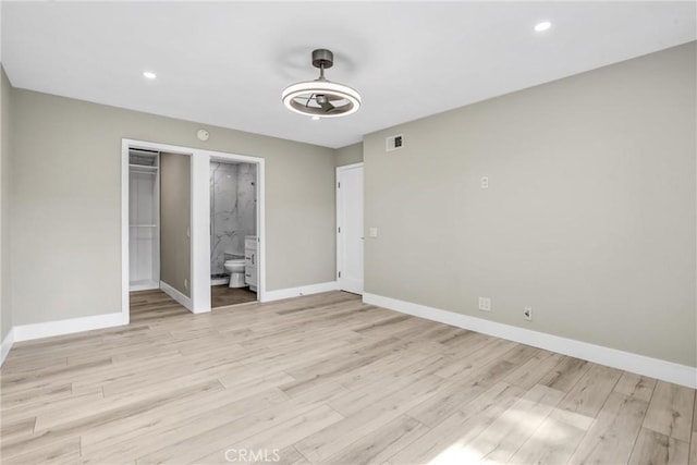 unfurnished bedroom featuring light wood-style floors, visible vents, connected bathroom, and baseboards