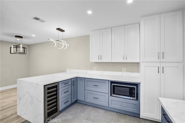 kitchen featuring wine cooler, pendant lighting, stainless steel microwave, white cabinets, and a peninsula