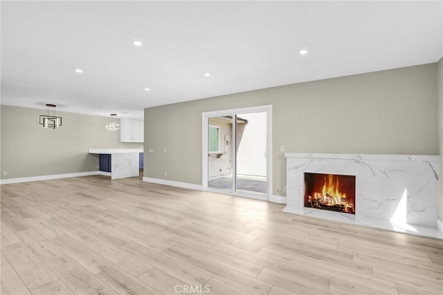 unfurnished living room with light wood-style flooring, a premium fireplace, baseboards, and recessed lighting