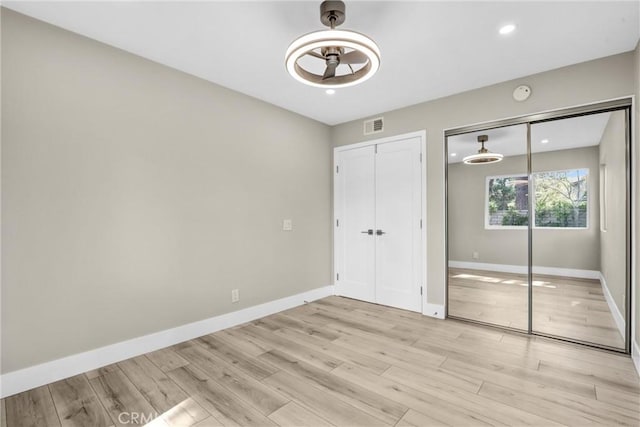 unfurnished bedroom with visible vents, light wood-style flooring, baseboards, and two closets