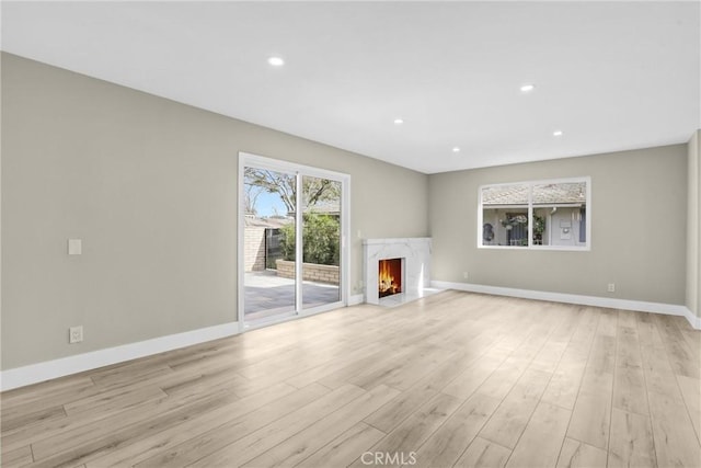 unfurnished living room featuring light wood-style flooring, recessed lighting, a high end fireplace, and baseboards