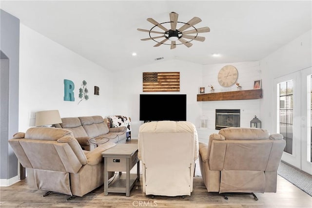 living area with light wood finished floors, visible vents, lofted ceiling, ceiling fan, and a fireplace