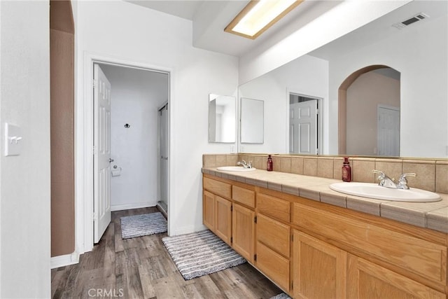 full bath featuring wood finished floors, a sink, visible vents, baseboards, and double vanity