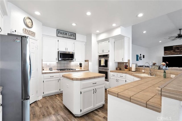 kitchen featuring stainless steel appliances, tile counters, white cabinetry, a kitchen island, and a peninsula