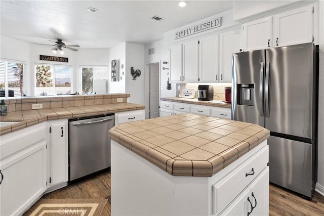 kitchen with tile countertops, a kitchen island, white cabinetry, and stainless steel appliances