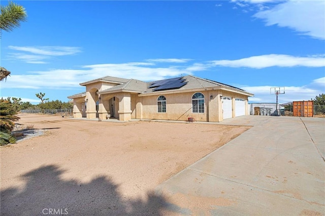 view of front of property with driveway, solar panels, an attached garage, fence, and stucco siding