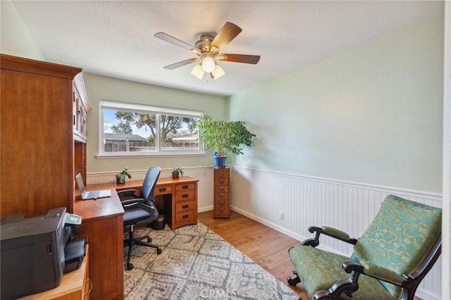 home office featuring light wood-style flooring, a ceiling fan, and wainscoting