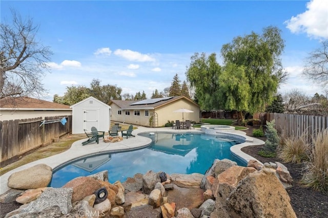 view of pool with an outbuilding, a pool with connected hot tub, a patio area, a shed, and a fenced backyard