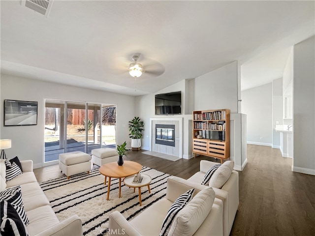 living room featuring ceiling fan, dark wood-type flooring, visible vents, baseboards, and a tiled fireplace