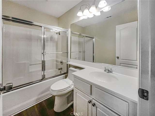 bathroom with toilet, bath / shower combo with glass door, wood finished floors, vanity, and visible vents