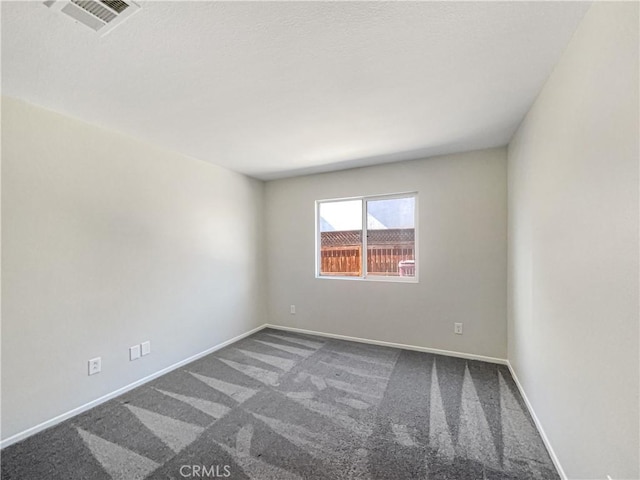 empty room featuring visible vents, dark carpet, and baseboards