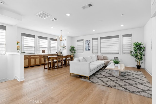 living area featuring light wood-style floors, visible vents, and a chandelier