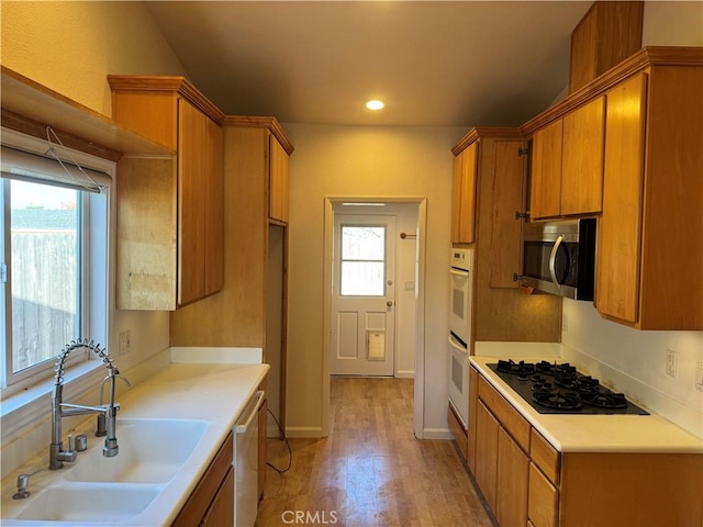 kitchen featuring stainless steel appliances, a sink, light countertops, light wood-type flooring, and brown cabinets