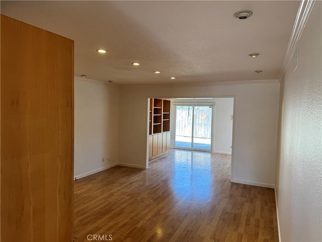 empty room with baseboards, a textured ceiling, wood finished floors, and crown molding