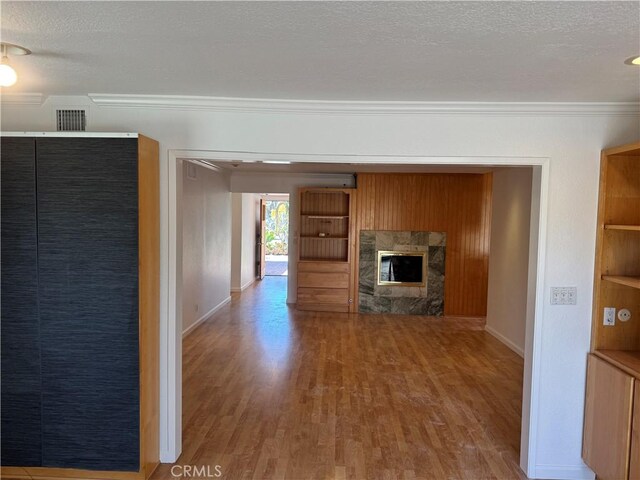 unfurnished living room featuring a textured ceiling, a premium fireplace, wood finished floors, visible vents, and crown molding