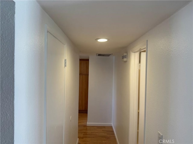 hall featuring visible vents, baseboards, and wood finished floors