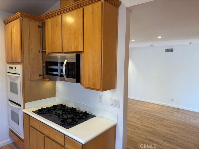 kitchen with double oven, black gas stovetop, visible vents, brown cabinets, and stainless steel microwave