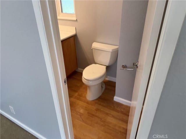 half bathroom with baseboards, vanity, toilet, and wood finished floors