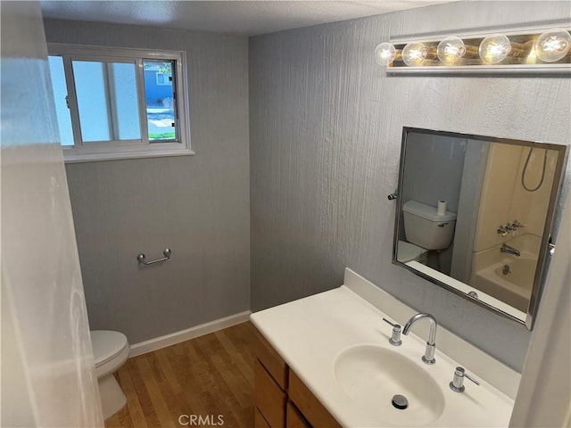 bathroom with a bathtub, toilet, vanity, wood finished floors, and baseboards