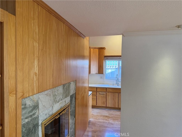 interior space with a textured ceiling, a tile fireplace, a sink, light wood-type flooring, and brown cabinetry