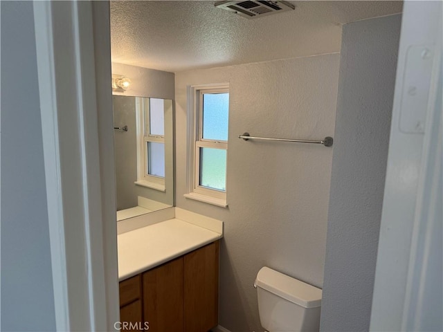 bathroom with visible vents, a textured wall, toilet, a textured ceiling, and vanity