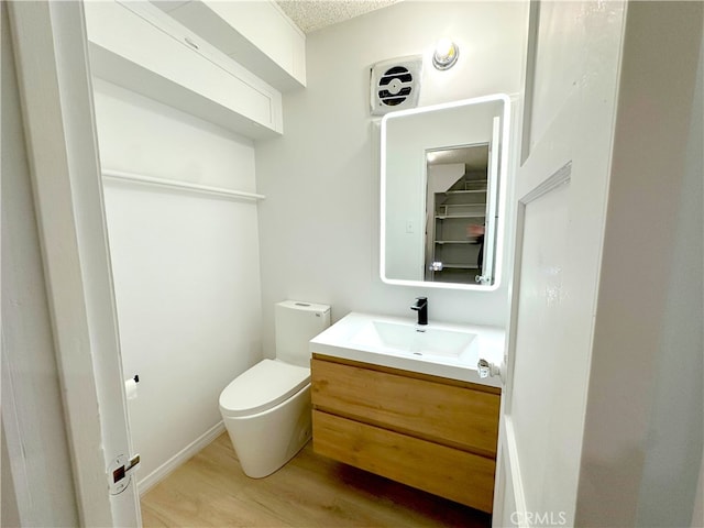 half bath with toilet, wood finished floors, and vanity